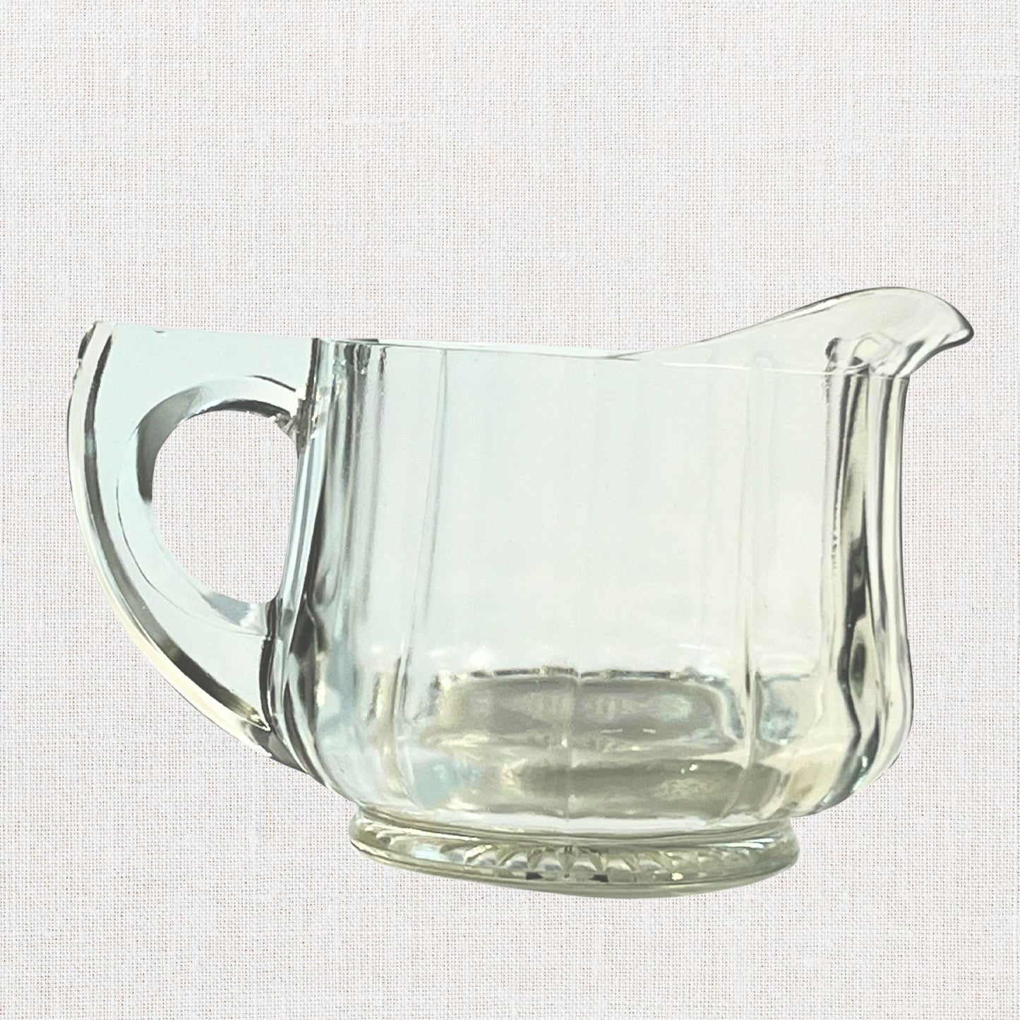 Clear glass ribbed creamer on neutral background, vintage home decor or collectible.