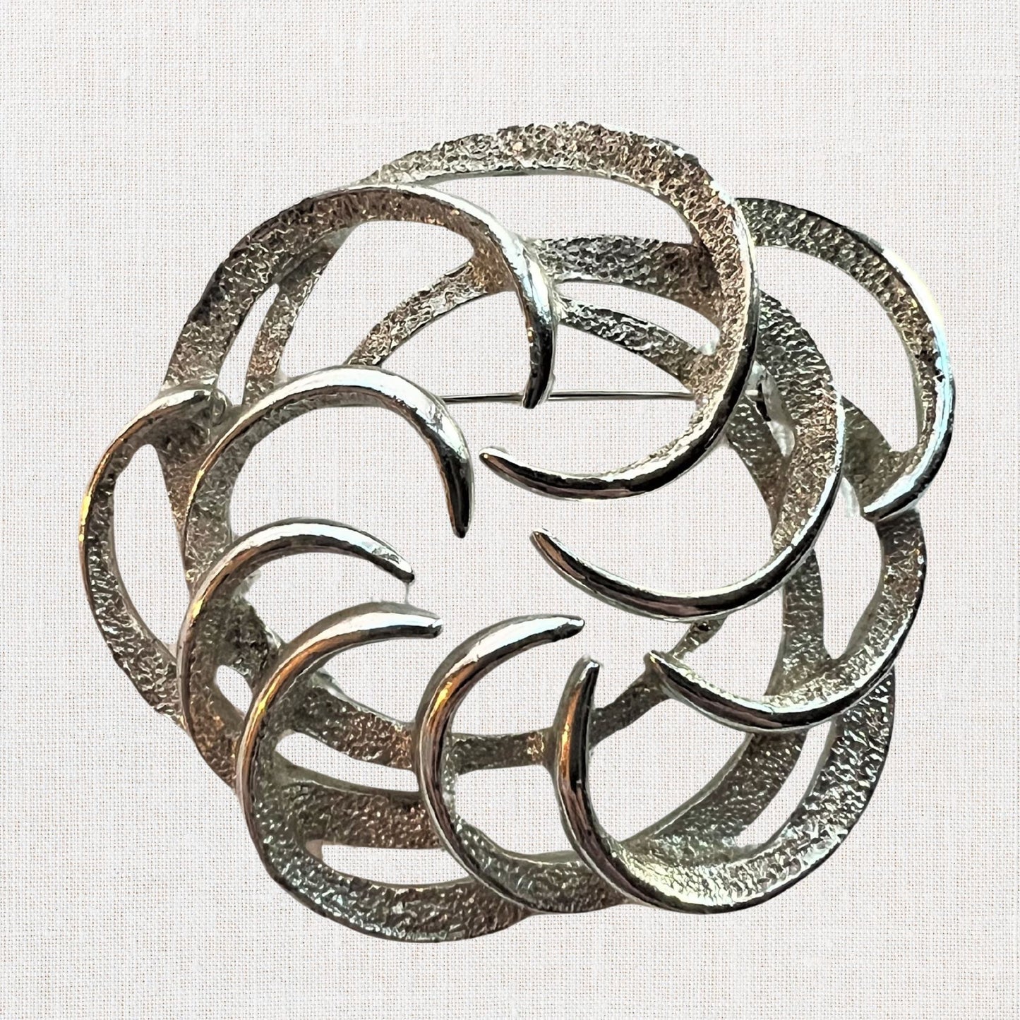 Silvertone interlocking circles brooch on neutral background, vintage home decor or collectible.