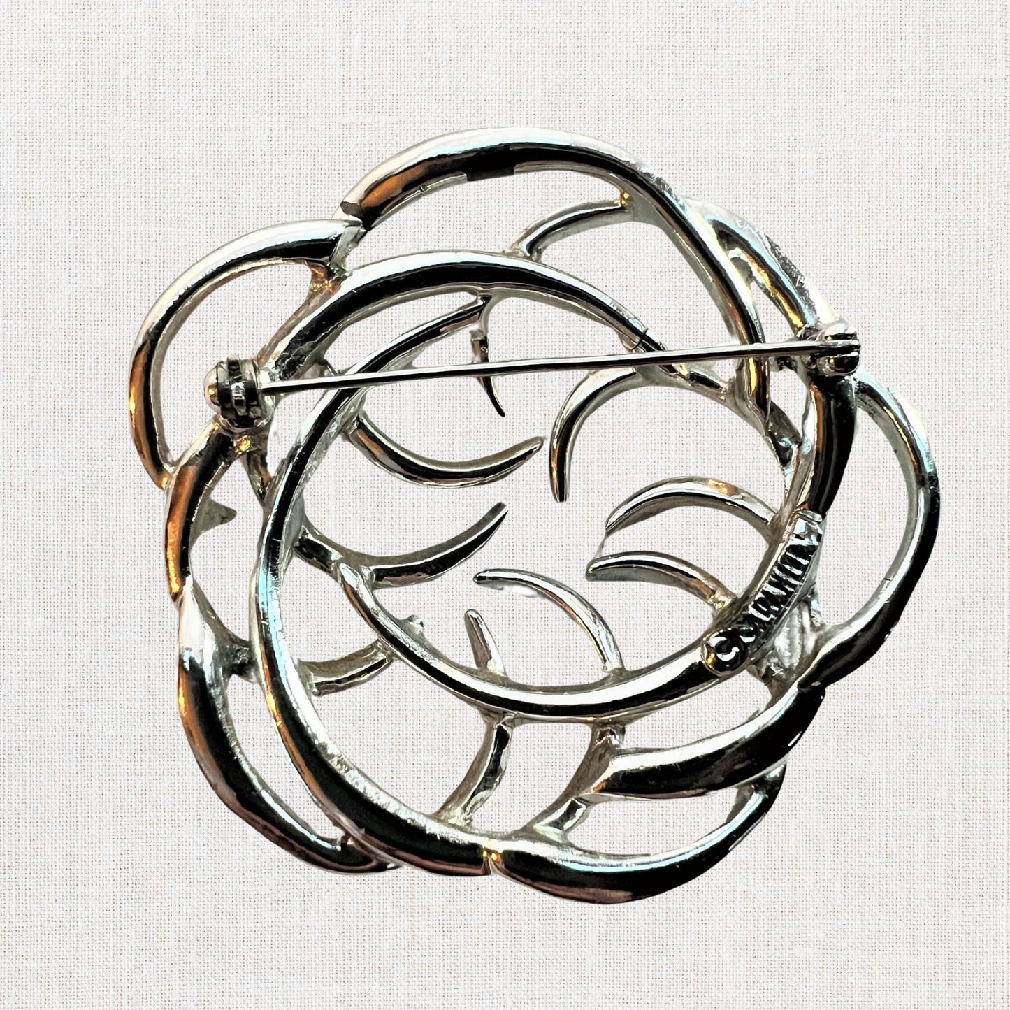 Silvertone interlocking circles brooch on neutral background, vintage home decor or collectible.