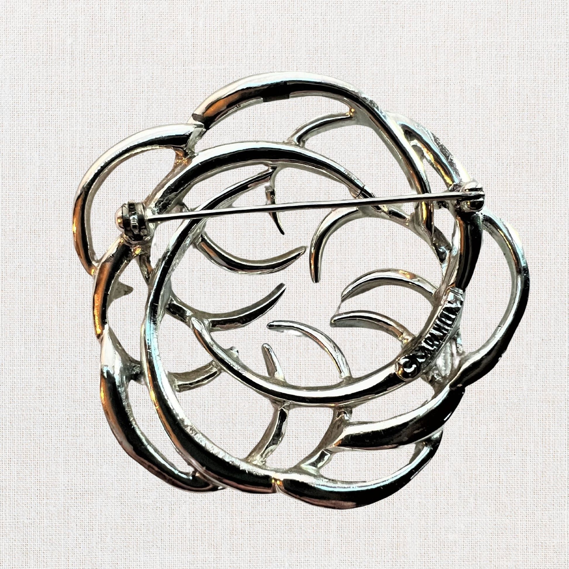 Silvertone interlocking circles brooch on neutral background, vintage home decor or collectible.