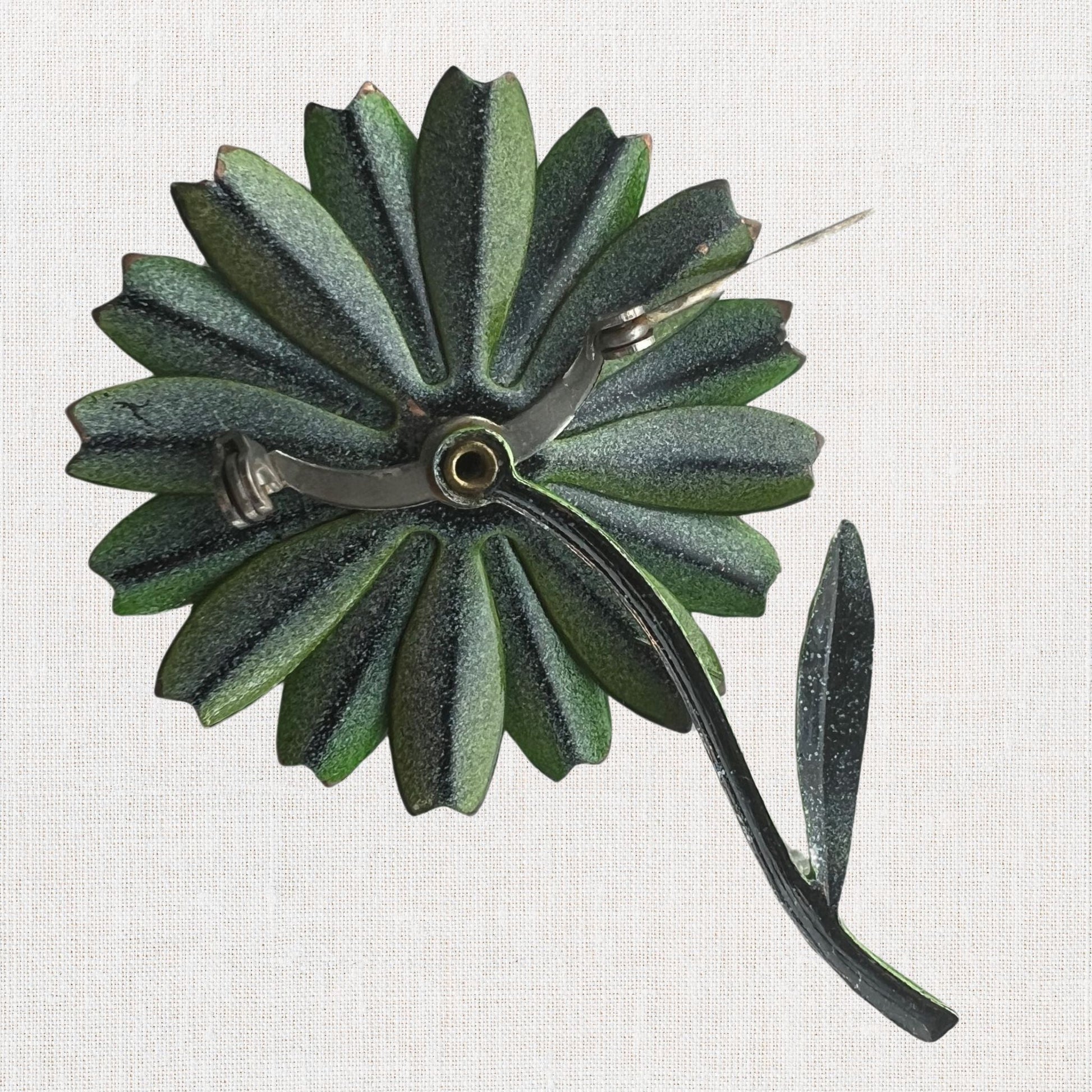 Green flower brooch with moveable stem on neutral background, vintage home decor or collectible.